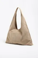 Bolso de hombro maxi de estructura blanda, exterior de serraje color beige claro, con cierre de cordón y logo metálico.