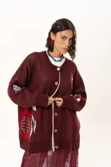 Saco de punto color vino con diseño holgado, cuello redondo y mangas largas. Presenta un gran bordado central en la espalda con forma de flor en tonos crema y rojo, acompañado de un pequeño bordado de sol y una frase bordada en la parte inferior.