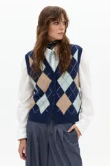 Chaleco de punto color azul marino con estampado de rombos en tonos beige, azul claro y lila. Tiene escote en V, botones frontales y terminaciones de rib.