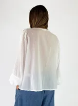 Blusa de algodón blanca con escote en V, mangas largas amplias y detalles de volados con encaje bordado en el frente.
