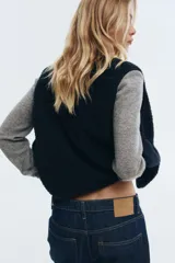 Chaleco de sherpa color negro, con cuello redondo y cierre frontal de botones a presión. Presenta bolsillos laterales de parche y ribetes finos en los bordes.