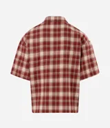 Camisa de franela de algodón con diseño a cuadros en tonos rojo y beige, de corte holgado relaxed, mangas cortas, cuello tradicional y cierre frontal con cremallera. Cuenta con un bolsillo aplicado en el pecho con detalle de botón metálico.