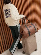 Bolso de viaje grande de cuero marrón con detalles en cuero negro, doble asa de mano y tiras decorativas verticales.