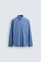 Camisa de corte regular fit confeccionada en tejido de algodón de color azul. Cuenta con cuello solapa, manga larga con puño abotonado, bolsillo de parche en el pecho y cierre frontal con botones.