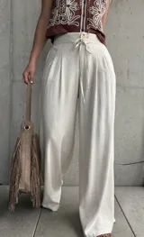 Pantalón palazo de lino color beige, de calce amplio y fluido, con tablas en el frente, botón, cierre y cordón ajustable en la cintura.