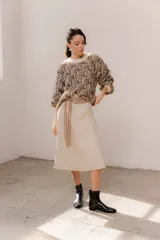 Pollera midi de eco cuero color beige, de corte recto y tiro alto, con costuras verticales decorativas y detalle de cinturón fino con flecos.