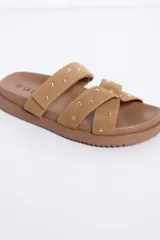 Sandalias planas color beige con dos tiras cruzadas en el empeine decoradas con tachas metálicas, suela ancha y diseño cómodo.