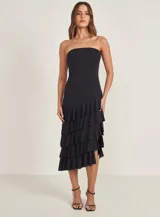 Vestido negro strapless con corte midi y falda con volados asimétricos.