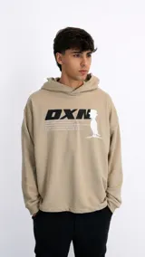 Hoodie color beige con capucha, de corte holgado y diseño oversize. Presenta un estampado gráfico frontal en color negro y blanco con el texto 'DXN' y una silueta de un personaje con sombrero.