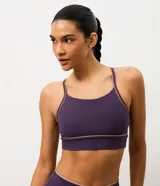 Top deportivo de microfibra en color violeta con detalles de friso en tono arena. Presenta un diseño de escote redondo, breteles finos y una banda inferior elástica que proporciona mayor sujeción. Incluye copas removibles para mayor comodidad.