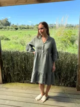 Vestido corto de lino color beige claro, con cuello mao, escote con botones de nácar, mangas tres cuartos con volados y ruedo con volado.