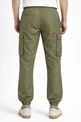 Pantalón cargo de nylon color beige, con elástico en la cintura y en los puños. Presenta bolsillos laterales con solapa y un logo de goma aplicado en uno de ellos.