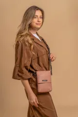 Phonebag pequeña color mostaza, confeccionada en cuero sintético, con solapa frontal y correa ajustable con logo de la marca.