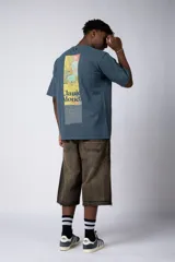 Remera de corte oversize color beige, confeccionada en algodón grueso. Presenta una estampa frontal pequeña con diseño artístico abstracto en tonos azules y amarillos.