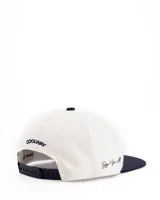 Gorra de béisbol blanca con visera plana azul marino y logo bordado en el frente.