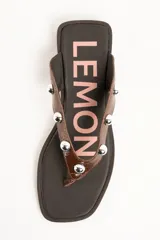 Sandalias tipo ojota de cuero marrón con acabado charol, con tiras decoradas con tachas metálicas esféricas y suela plana.