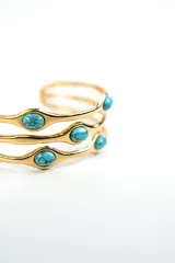 Brazalete rígido de metal plateado con diseño de tres tiras onduladas adornadas con piedras turquesas ovaladas.