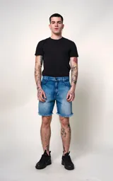 Bermuda de denim azul con efecto desgastado y roturas en ambas piernas. Presenta bordes deshilachados y un forro estampado visible en las aberturas. Tiene cierre frontal con botón metálico y cinco bolsillos.