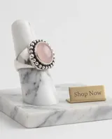 Anillo de plata 925 con piedra de cuarzo rosa natural en forma ovalada, rodeada por un diseño de pequeñas esferas metálicas.