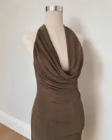 Vestido midi de color marrón, con escote halter profundo y diseño drapeado en la parte frontal. Presenta un tajo lateral con cordón ajustable y espalda descubierta.