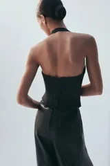 Top estilo corsé color beige, con escote recto, cuello halter y bajo asimétrico. Presenta costuras estructuradas frontales.