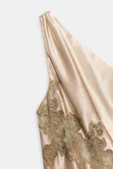 Vestido midi de satén en color beige con escote asimétrico de un solo hombro. Presenta aplicaciones de encaje a tono en el cuerpo y en el bajo, con un diseño de corte asimétrico.