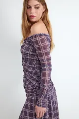 Top off-shoulder de manga larga con estampado de cuadros en tonos morados y beige. Confeccionado en tejido elástico y ligero, presenta un diseño fruncido en la parte frontal con cierre de botones.