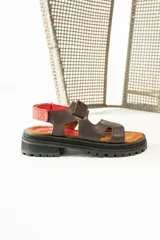 Sandalias de cuero marrón con diseño de tiras anchas y ajuste mediante velcro. Presentan una plantilla acolchada color tostado con detalles en rojo y una suela de goma negra con plataforma dentada.