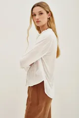 Camisa de algodón y viscosa color blanco, con mangas largas y diseño frontal con bordados geométricos y florales en contraste negro. Presenta cuello redondo con pequeña abertura y cierre frontal de botones.
