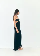 Vestido largo de fiesta color negro, con diseño recto y tirantes finos. Presenta un escote pronunciado y detalles cut-out en los laterales, con un bajo asimétrico y forro interior.