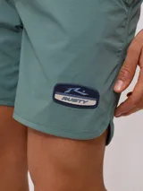 Short de baño tipo volley color verde azulado, con cintura elástica y cordón de ajuste en color azul marino. Presenta un parche con el logo de la marca en la pierna izquierda y aberturas laterales en el ruedo.