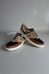 Championes de diseño urbano con combinación de tonos marrones, negros y detalles metalizados, puntera de cuero y suela blanca.