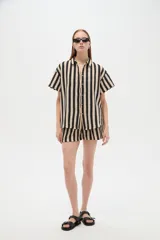 Camisa de algodón de corte holgado, con diseño de rayas verticales en colores negro y beige, cuello camisero y cierre frontal con botones.