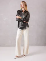 Camisa de manga larga con acabado satinado y efecto metalizado en color gris oscuro. Presenta cuello camisero clásico, cierre frontal con botones forrados y puños estructurados.