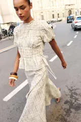 Blusa de manga corta abullonada con diseño a cuadros, cuello con volante y acabados elásticos. Cuenta con aberturas y lazos ajustables en los laterales.