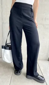 Pantalón negro de lino, de corte ancho y largo, con diseño suelto y botones decorativos en la cintura.