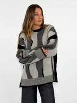 Sweater de tejido de punto con diseño de rayas verticales irregulares en tonos gris claro, gris oscuro y negro. Presenta cuello redondo, mangas largas con puños acanalados y aberturas laterales en el ruedo.
