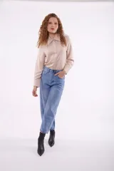 Camisa color beige con cuello clásico, cierre frontal con botones y detalle de flecos metálicos en el cuello.