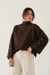 Sweater de bremer color chocolate con cuello alto y mangas largas con detalle de botones en los puños. Presenta un diseño holgado con aberturas laterales en el ruedo.