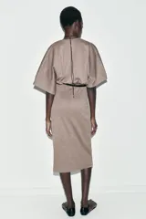 Vestido midi de tejido piqué en color marrón oscuro jaspeado, con escote en pico cruzado y mangas cortas. Presenta detalle de frunces en la cintura y un cinturón integrado con hebilla metálica a contraste.