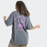 Remera de corte oversize color gris, con cuello redondo y mangas cortas. Presenta un estampado pequeño en el centro del pecho con motivos florales y de frutas en color rosado.