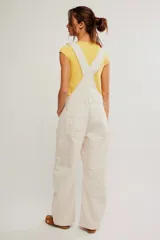 Jardinero de denim color blanco crudo, con peto, tiras ajustables y botones metálicos. Presenta diseño de pierna amplia tipo barrel, bolsillos frontales y traseros, con costuras pespuntadas visibles.