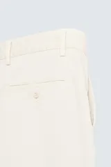 Pantalón chino de algodón color crema, corte regular fit, con cierre frontal de cremallera y botón, bolsillos delanteros y bolsillos traseros de vivo con botón.