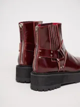 Bota corta de cuero negro tipo biker, con suela track de goma, plataforma, costuras y bordados decorativos en hilo rojo. Presenta tiras con hebillas metálicas y cierre en la parte trasera.