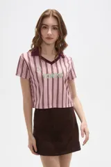 Remera estilo jersey de fútbol con corte cropped, cuello en V y mangas cortas. Presenta un diseño de rayas verticales en tonos rosados y bordó, con estampado frontal que incluye el texto 'TOKYO' y el número '24'.