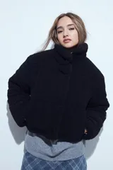 Campera puffer de corderito negro con cuello alto y diseño oversized. Presenta una textura tipo teddy, cierre frontal y corte a la cintura.