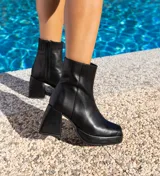 Botas cortas negras de cuero vacuno con textura tipo cocodrilo. Taco de madera forrado en cuero de 8cm, entre suela de goma de 2cm forrada en cuero, inclinación de horma de 6cm y caña de 15cm. Cierre YKK del lado interno y horma de punta cuadrada.