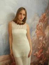 Vestido largo de punto color blanco con sutil brillo, escote redondo adornado con flores de cuero genuino y espalda descubierta.