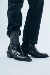 Bota de caña media confeccionada en cuero negro con acabado brillante, diseño de silueta limpia, puntera cuadrada y taco cuadrado de altura media.