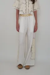 Pantalón blanco de lino con cintura elastizada, cordón de ajuste, bolsillos laterales y apliques de flores bordadas en los laterales.